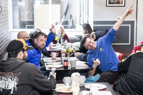 Group of people sitting at a dining table in a community centre. Some people are smiling at the camera