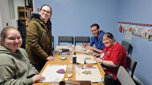 3 volunteers and 1 client sitting at a table doing crafts all smiling and lookig at the camera