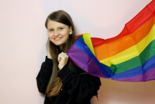 A smiling young person with the Pride flag over thier shoulders