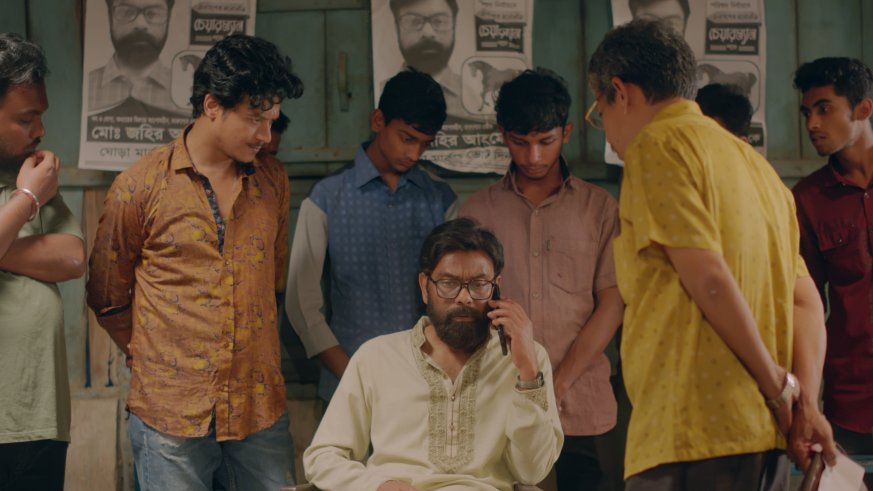 A man is sitting and talking on a phone surrounded by other men