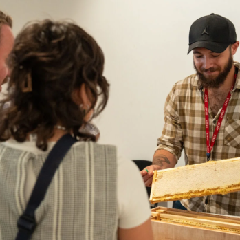A man is showing a group of people how honey is made from a beehive