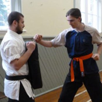 Karate instructor holding punching mat while student practices
