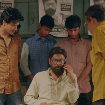 A man is sitting and talking on a phone surrounded by other men