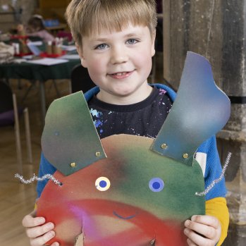 A photo of a boy holding a sculpture he has made. It is made out of various coloured card and materials.