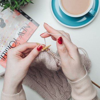 Photo of hands knitting, with a cup of tea by the side